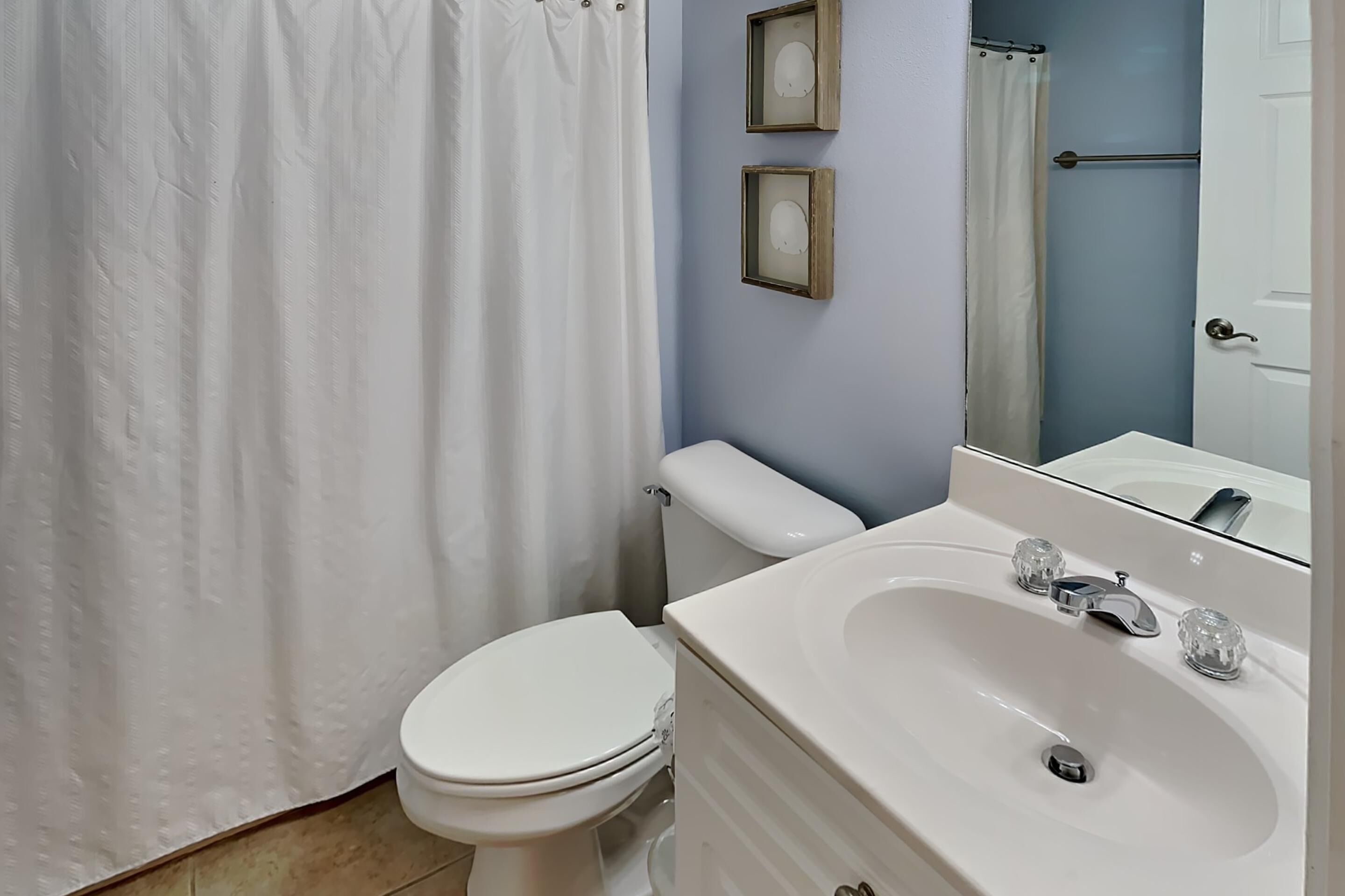A bathroom with a white toilet, a white sink with a mirror above it, and a shower curtain.
