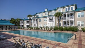 Um hotel com piscina, espreguiçadeiras e um edifício de dois andares com varandas.