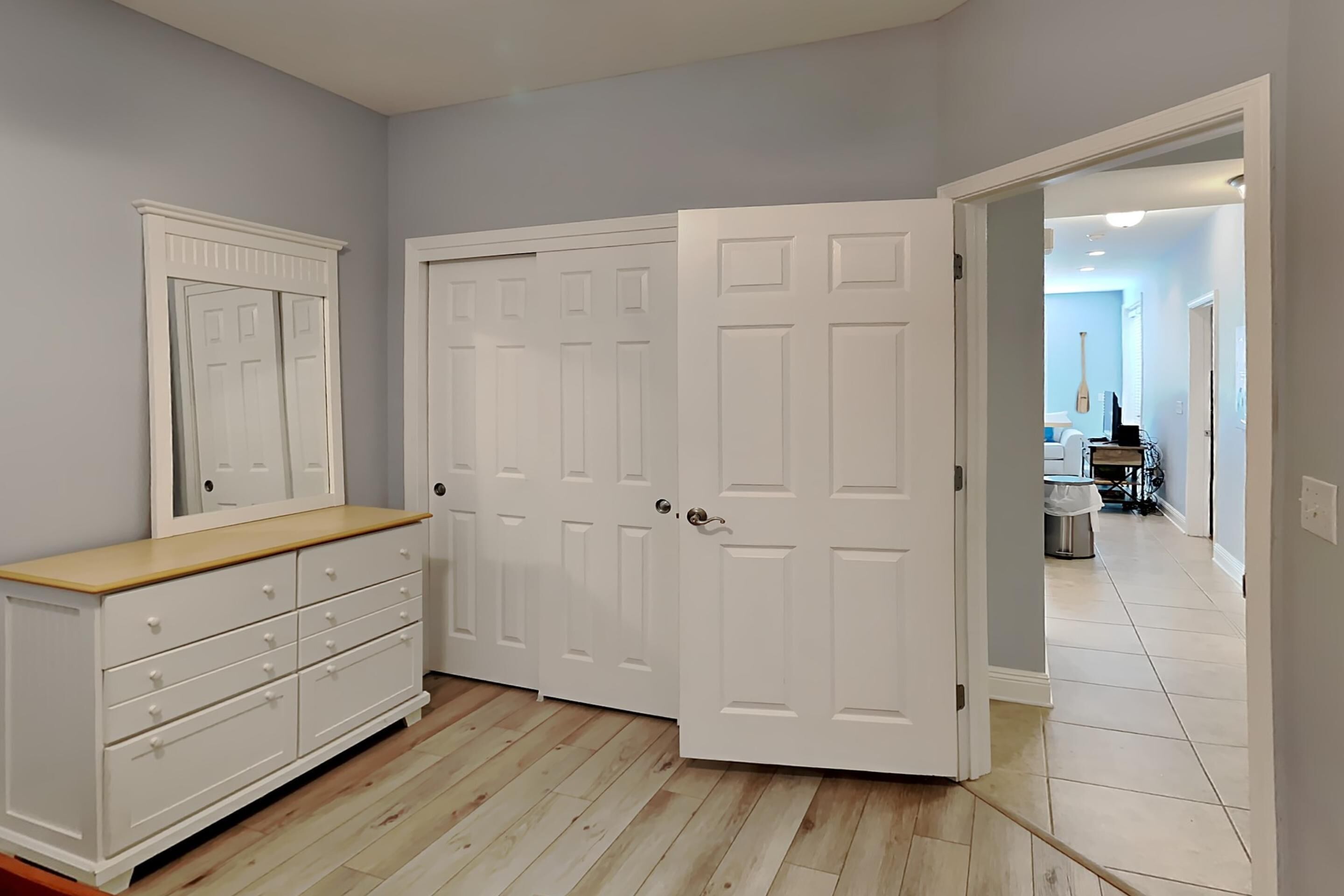 A room with a white dresser, a large mirror, and a white door.