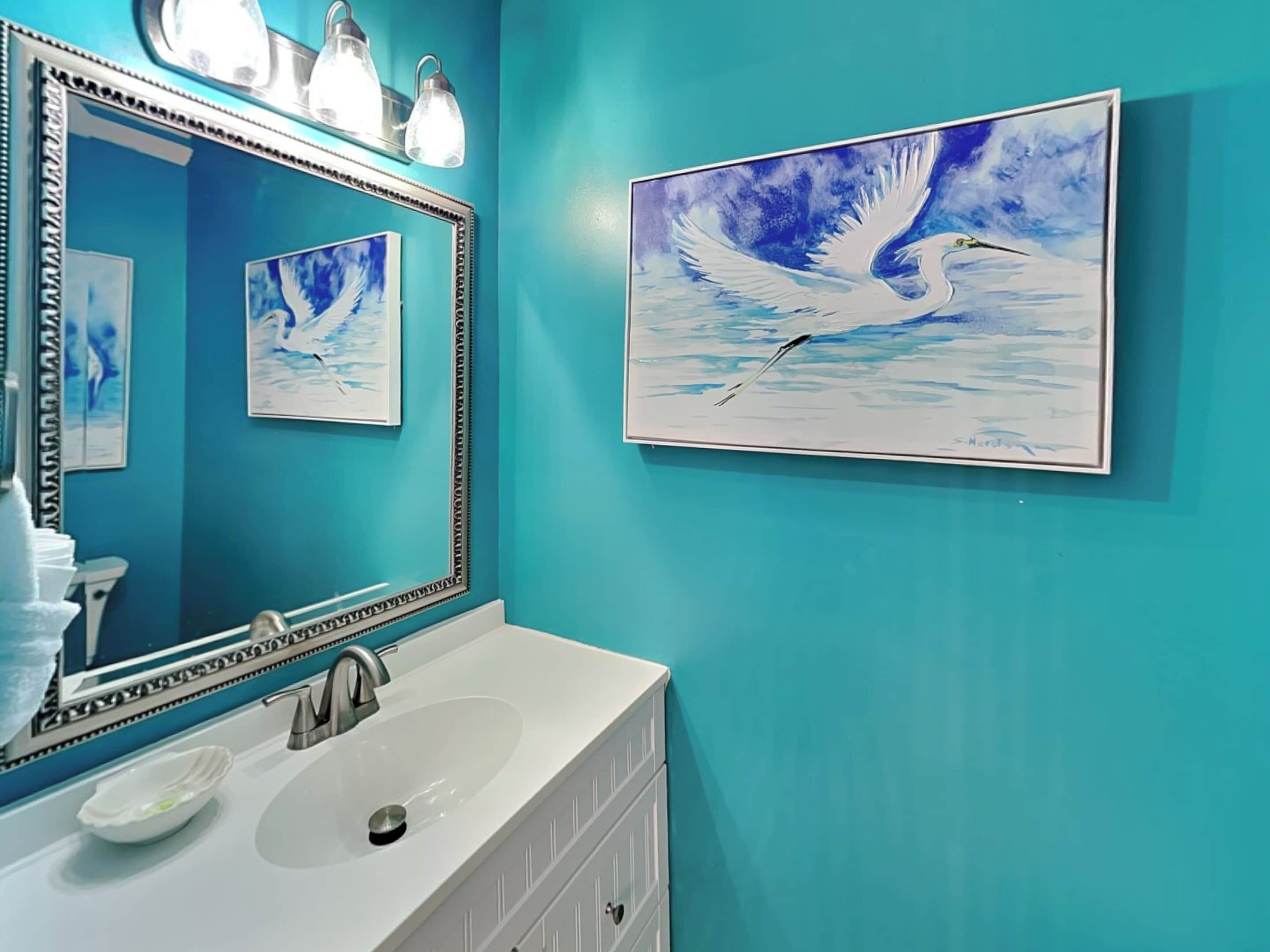 A bathroom with a large mirror, a sink, and a teal wall. There are framed pictures of birds on the wall.