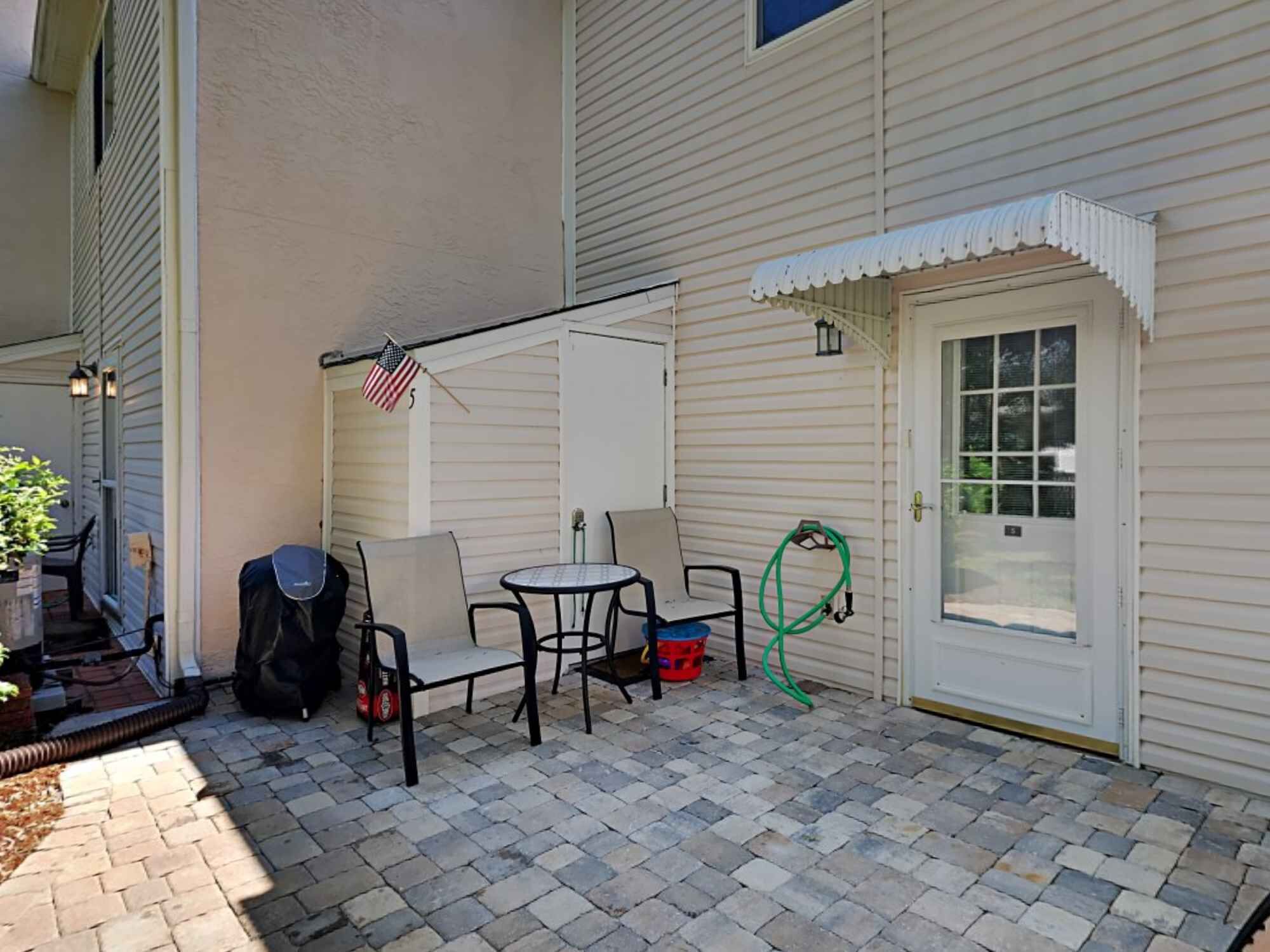 A patio with a table and chairs, a grill, and a hose.