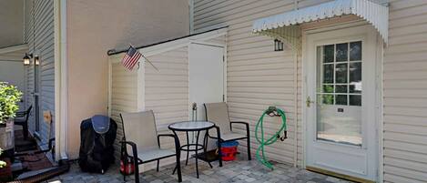 A patio with a table and chairs, a grill, and a hose.
