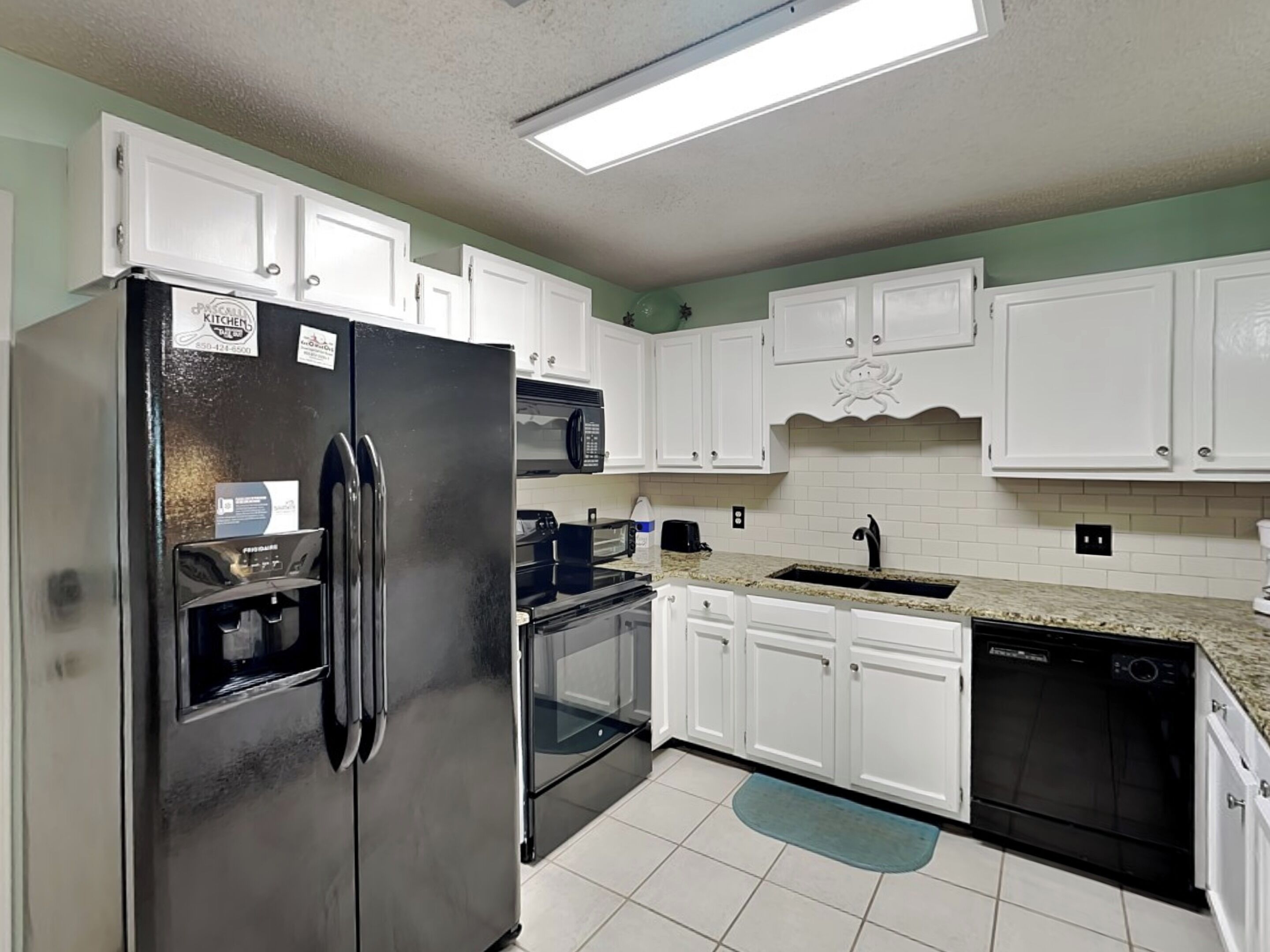 A kitchen with white cabinets, a stainless steel refrigerator, a microwave, a toaster, and a dishwasher.