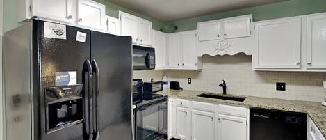 A kitchen with white cabinets, a stainless steel refrigerator, a microwave, a toaster, and a dishwasher.