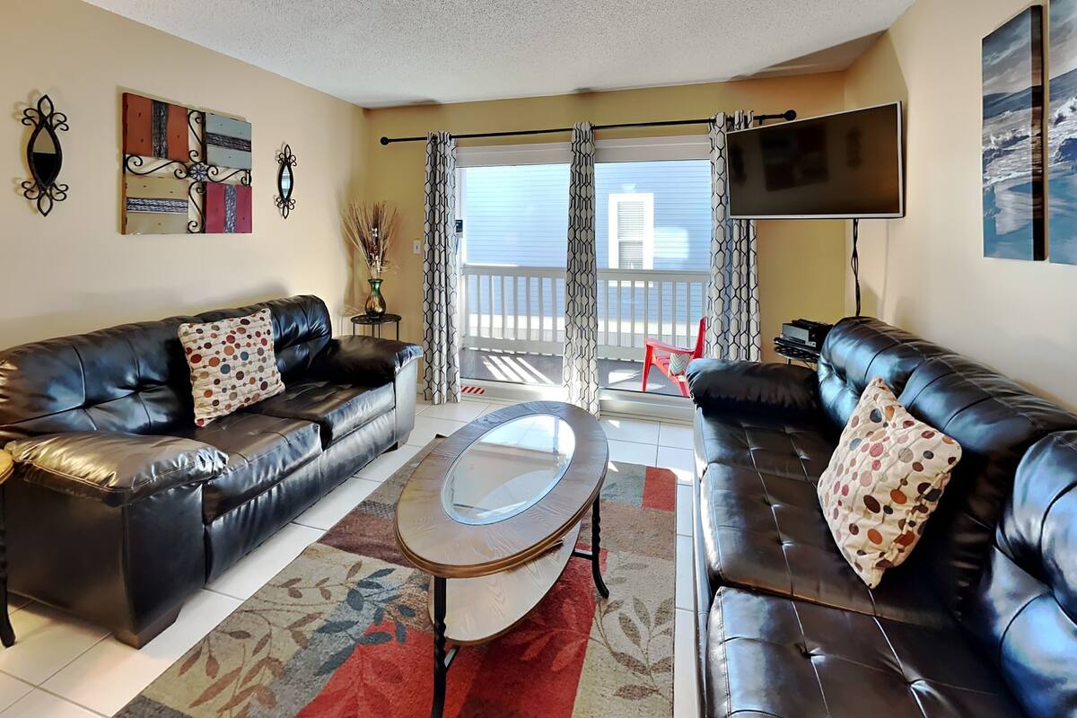 A living room with two black leather sofas, a glass coffee table, and a large flat-screen TV.