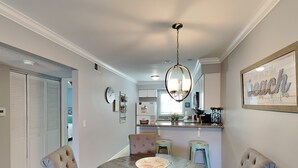 A dining area with a round table, cushioned chairs, a chandelier, and a kitchen in the background. - Villas on the Gulf Breeze by Southern Vacation Rentals (Pensacola Beach)