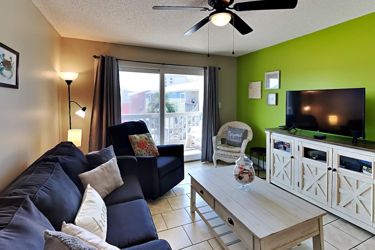 A living room with a dark blue sofa, a white cabinet with a TV, and a ceiling fan.