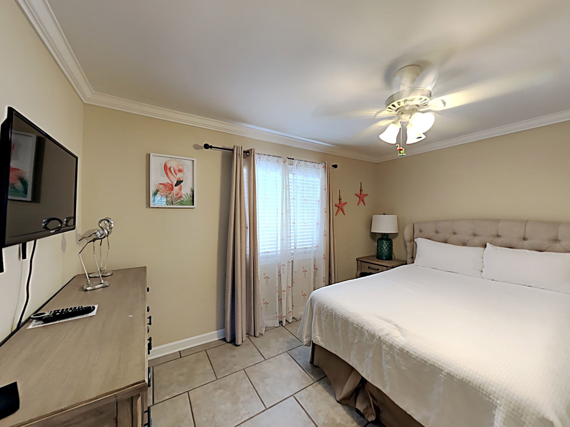 A hotel room with a bed, a desk with a computer, a TV, and a ceiling fan.