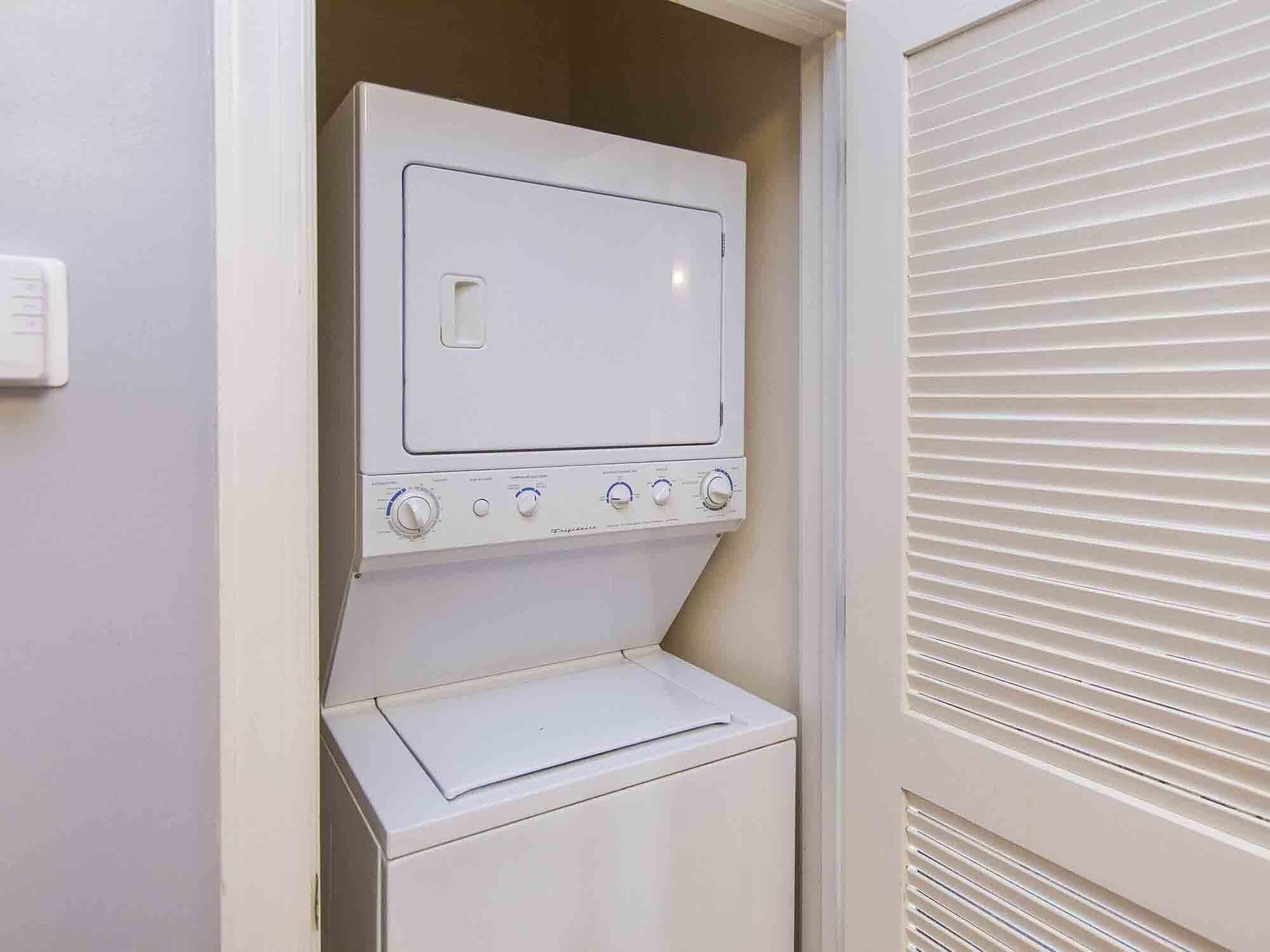 A compact laundry room with a built-in washer and dryer, a control panel with multiple dials, and a small shelf.