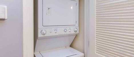 A compact laundry room with a built-in washer and dryer, a control panel with multiple dials, and a small shelf.