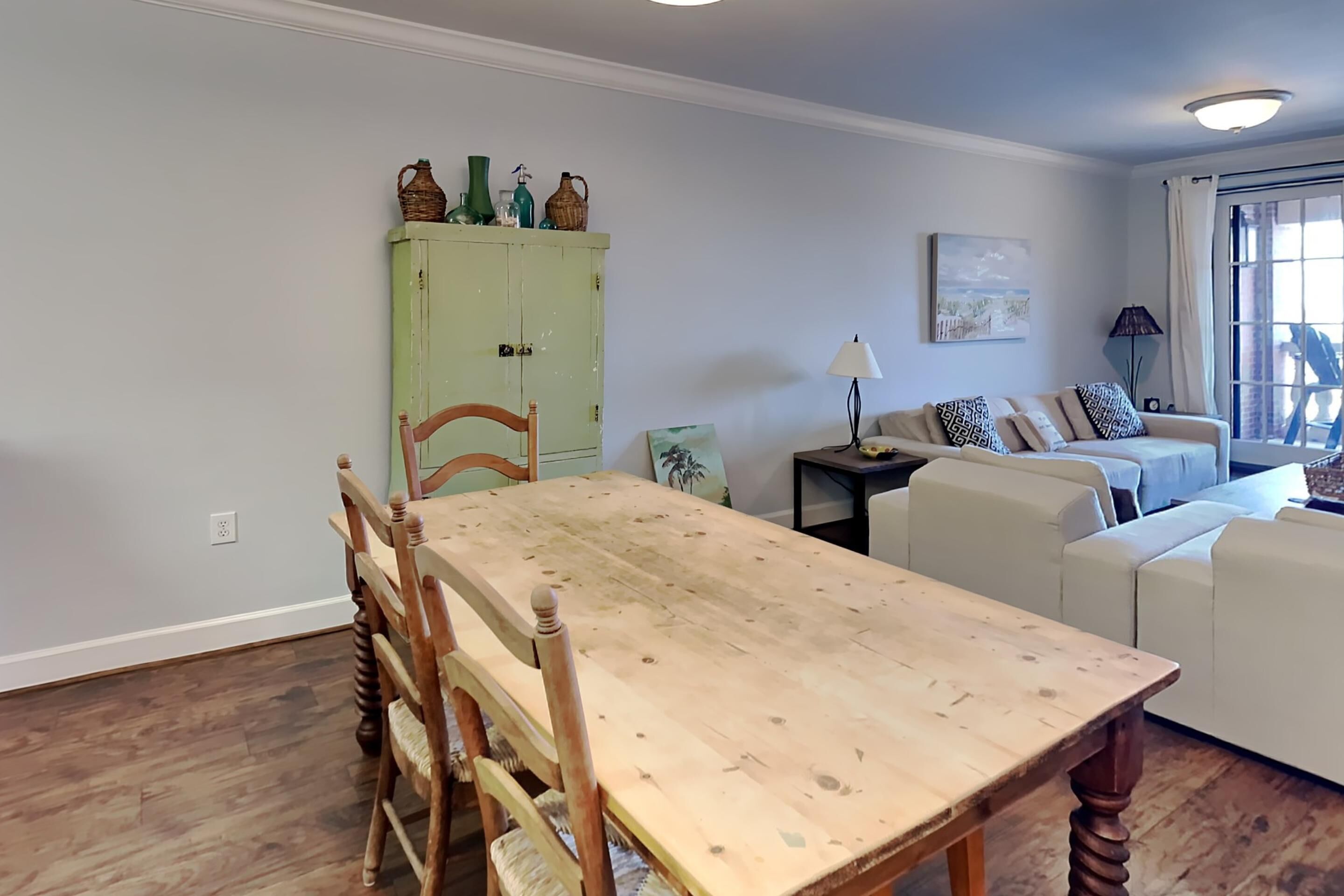 Un comedor con una mesa y sillas de madera, un armario verde con objetos decorativos, un sofá y una lámpara.