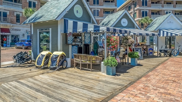 A beachfront boardwalk with a row of beachside shops, including a bike rental service and a café.