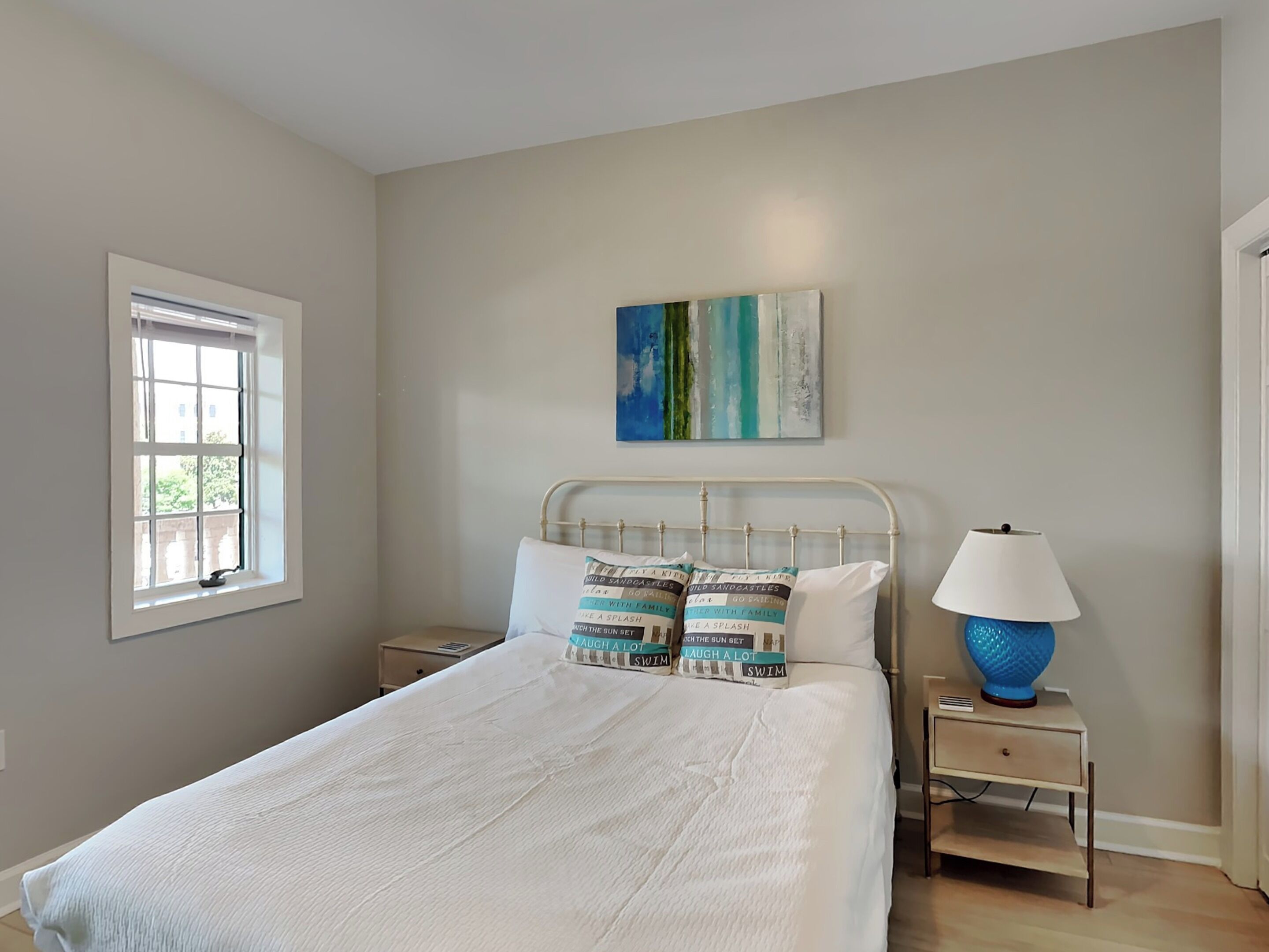 Un dormitorio con cama, mesita de noche, lámpara y ventana.
