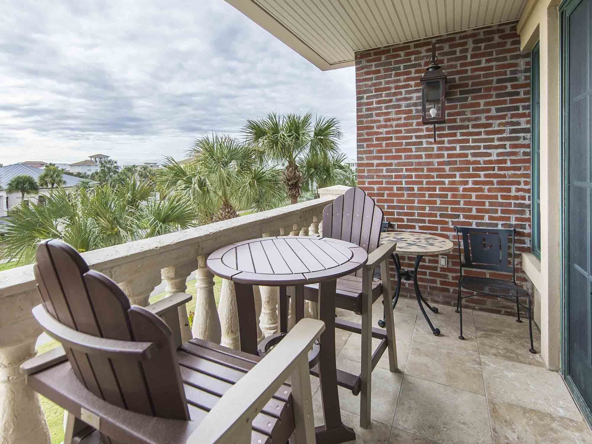 A balcony with a brick wall, two Adirondack chairs, a round table, and a small round table with a chair.