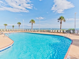 A clear blue pool with a white fence, palm trees, and a view of the ocean.