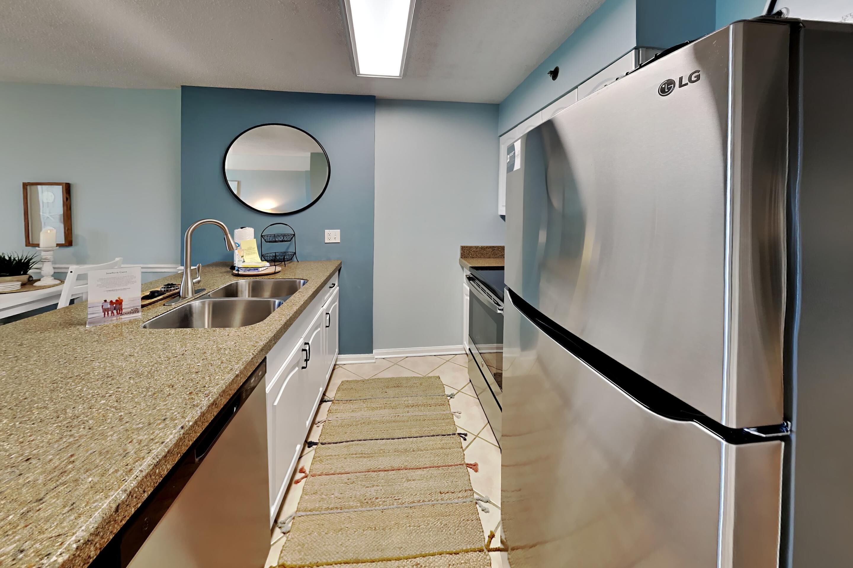 A kitchen with a stainless steel refrigerator, a granite countertop, a sink, and a mirror.