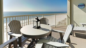Ein Balkon mit einem runden Tisch und vier Adirondack-Stühlen, mit Blick auf einen Strand und das dahinterliegende Meer.
