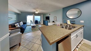 Eine moderne Küche mit Granit Arbeitsplatten, ein Essbereich mit Tisch und Stühlen, ein Wohnzimmer mit Sofa und Fernseher sowie ein Balkon mit Aussicht.