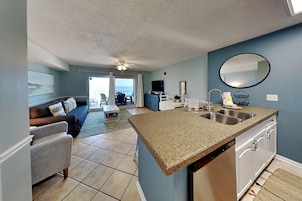 A modern kitchen with granite countertops, a dining area with a table and chairs, a living room with a sofa and a TV, and a balcony with a view.