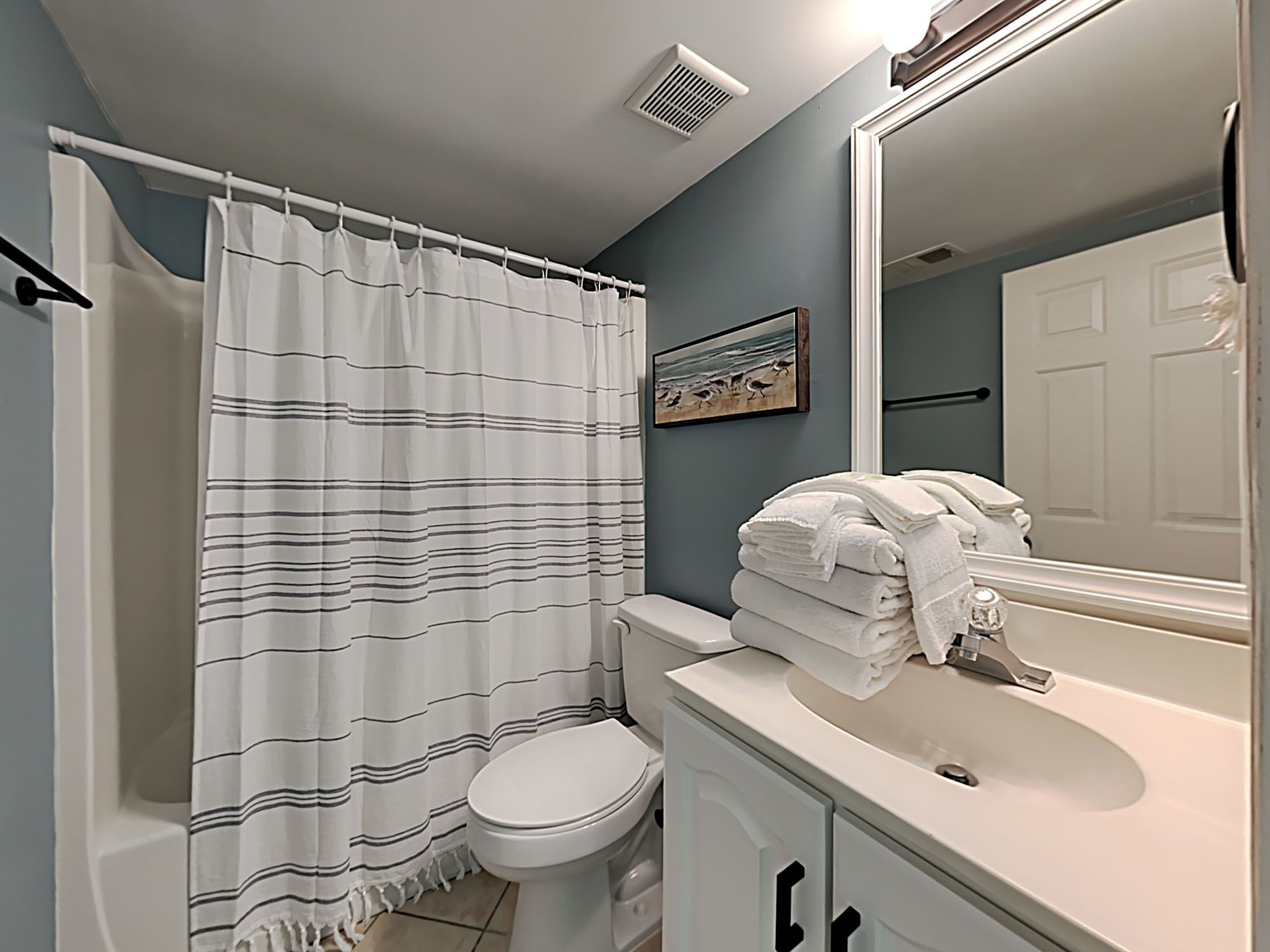 A bathroom with a striped shower curtain, a toilet, a sink with stacked towels, and a mirror.