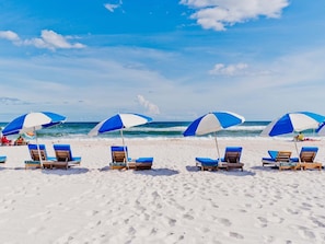 Una playa con hileras de sombrillas azules y blancas y sillas de playa.