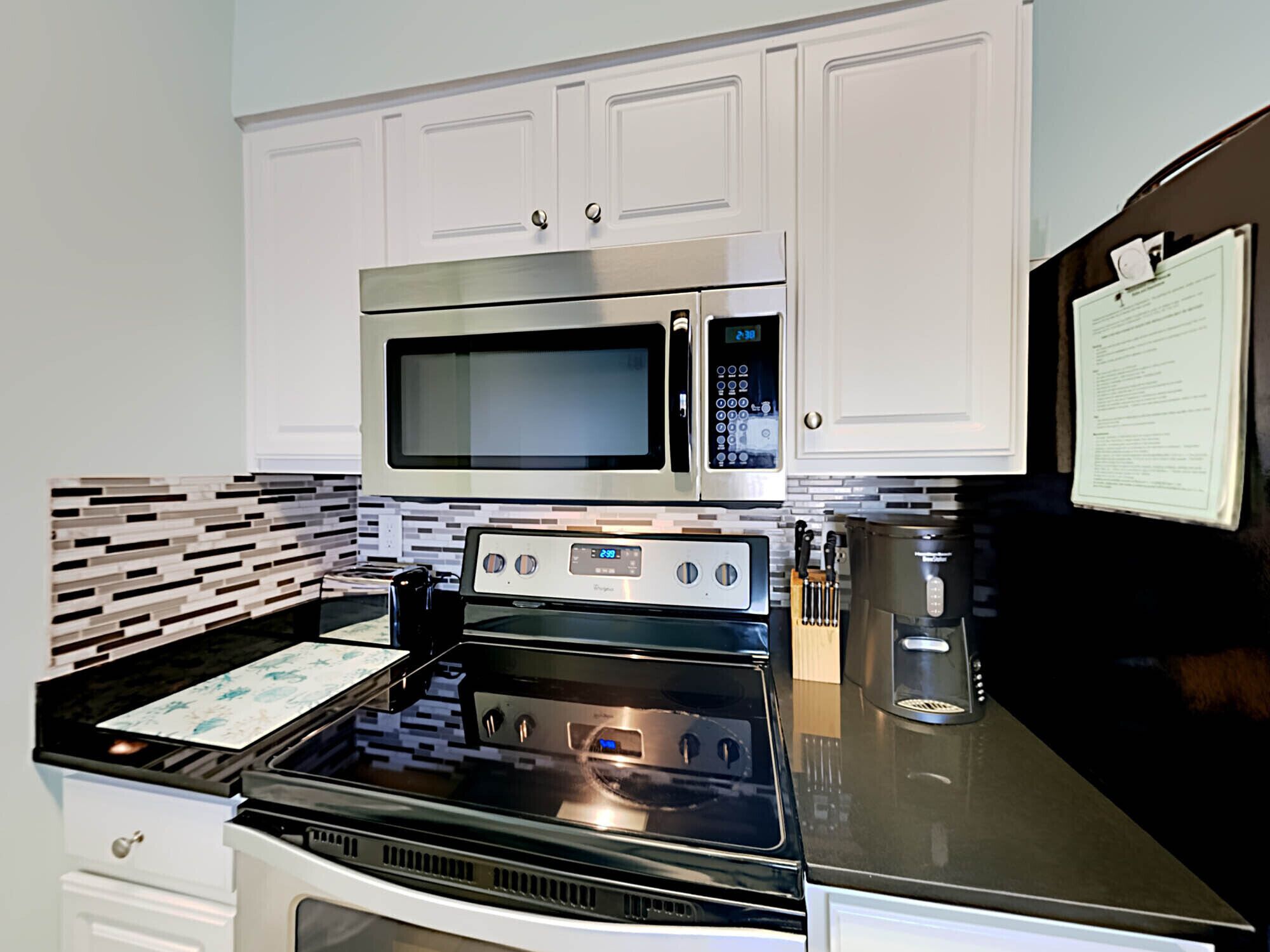 A modern kitchen with white cabinets, a stainless steel microwave, a gas stove, and a coffee maker.