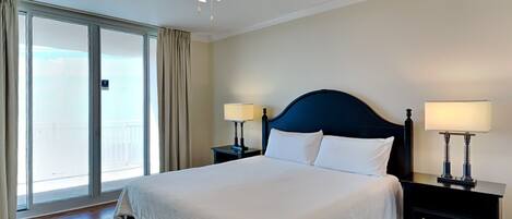 A hotel room with a large bed, two bedside tables with lamps, a ceiling fan, and a sliding glass door to a balcony.