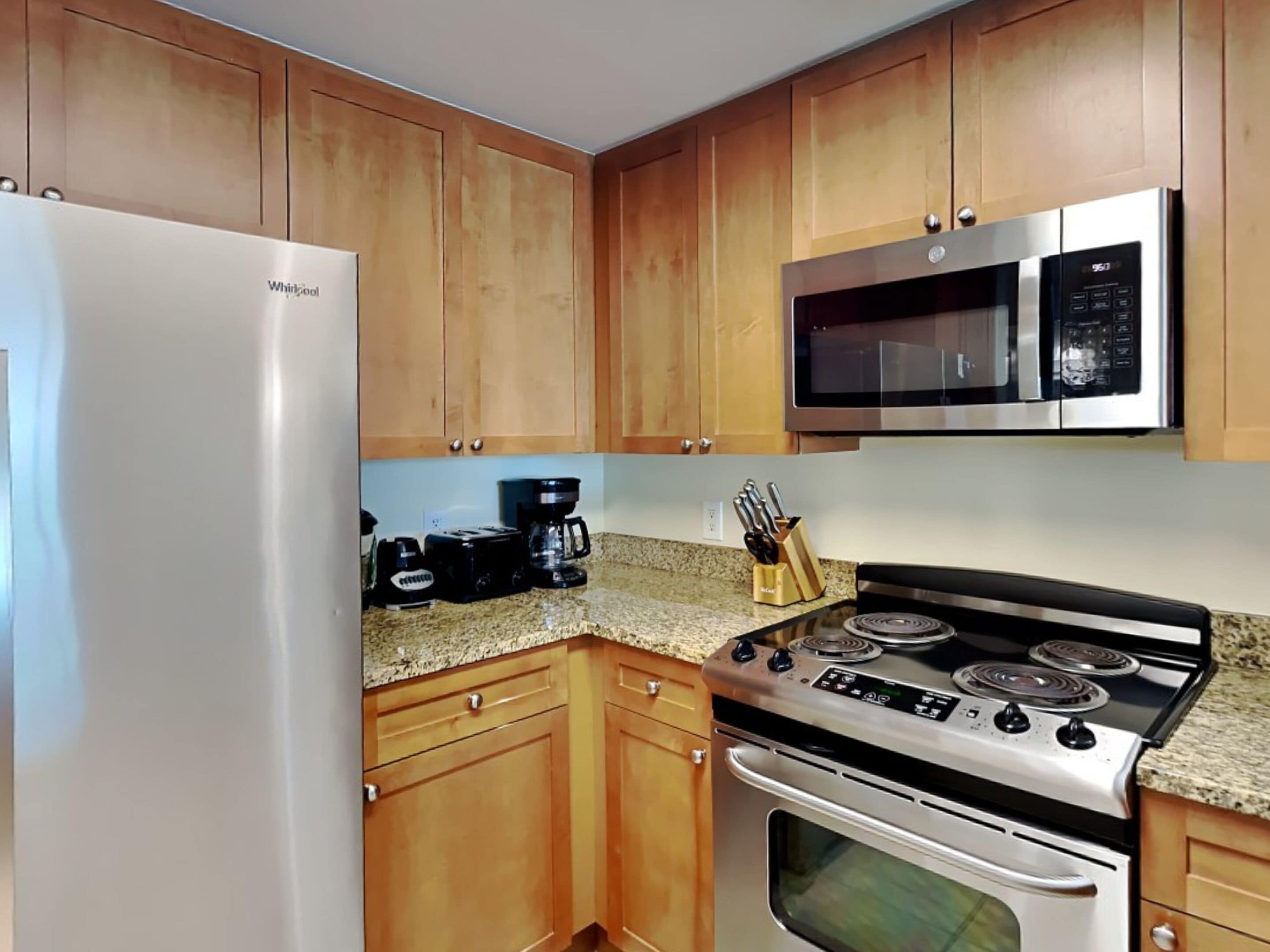 A kitchen with wooden cabinets, a stainless steel refrigerator, a microwave, a coffee maker, and a stove.
