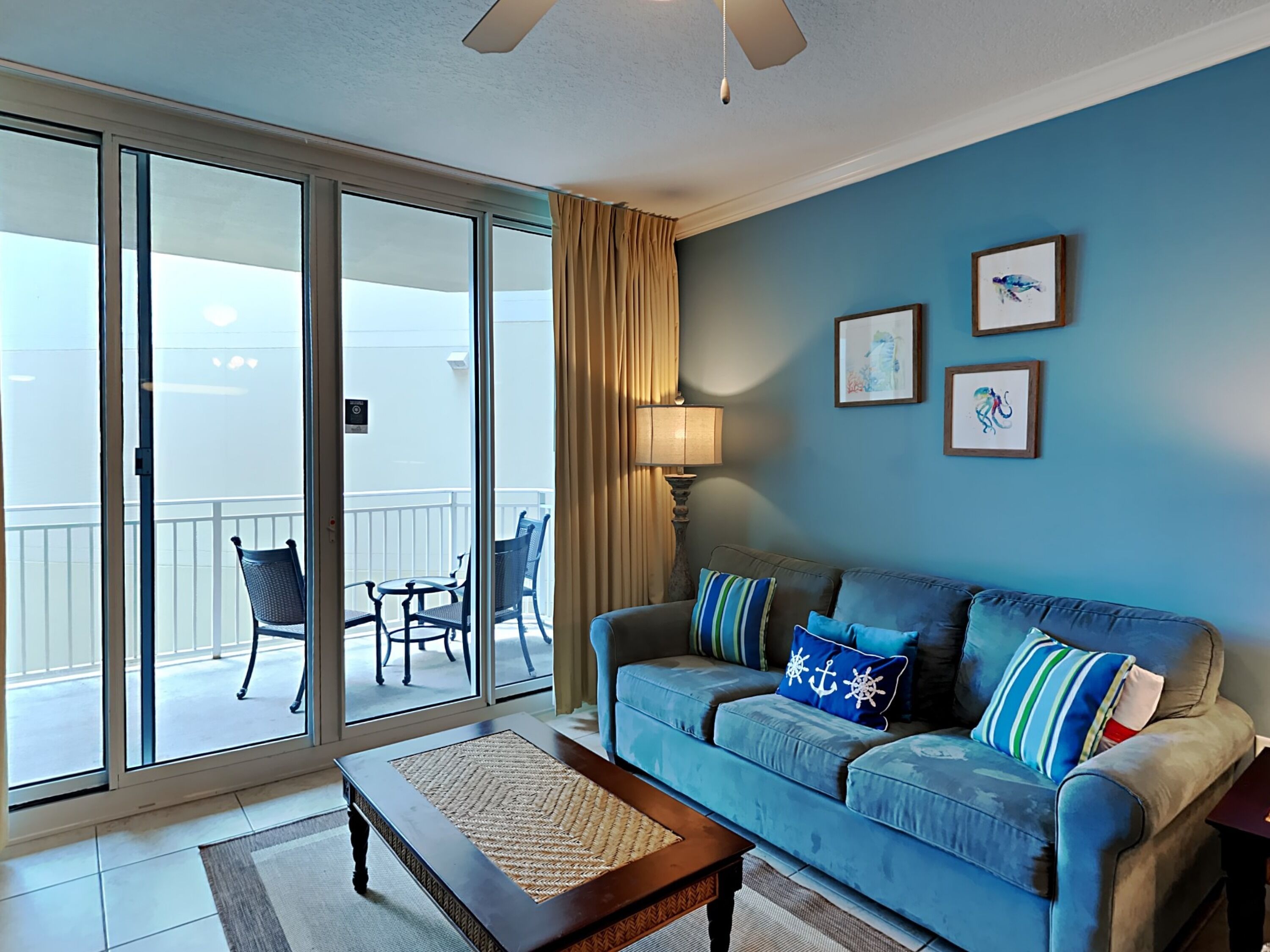 Un salon avec un canapé bleu, une table basse et une vue sur un balcon agrémenté de chaises et d’une table.