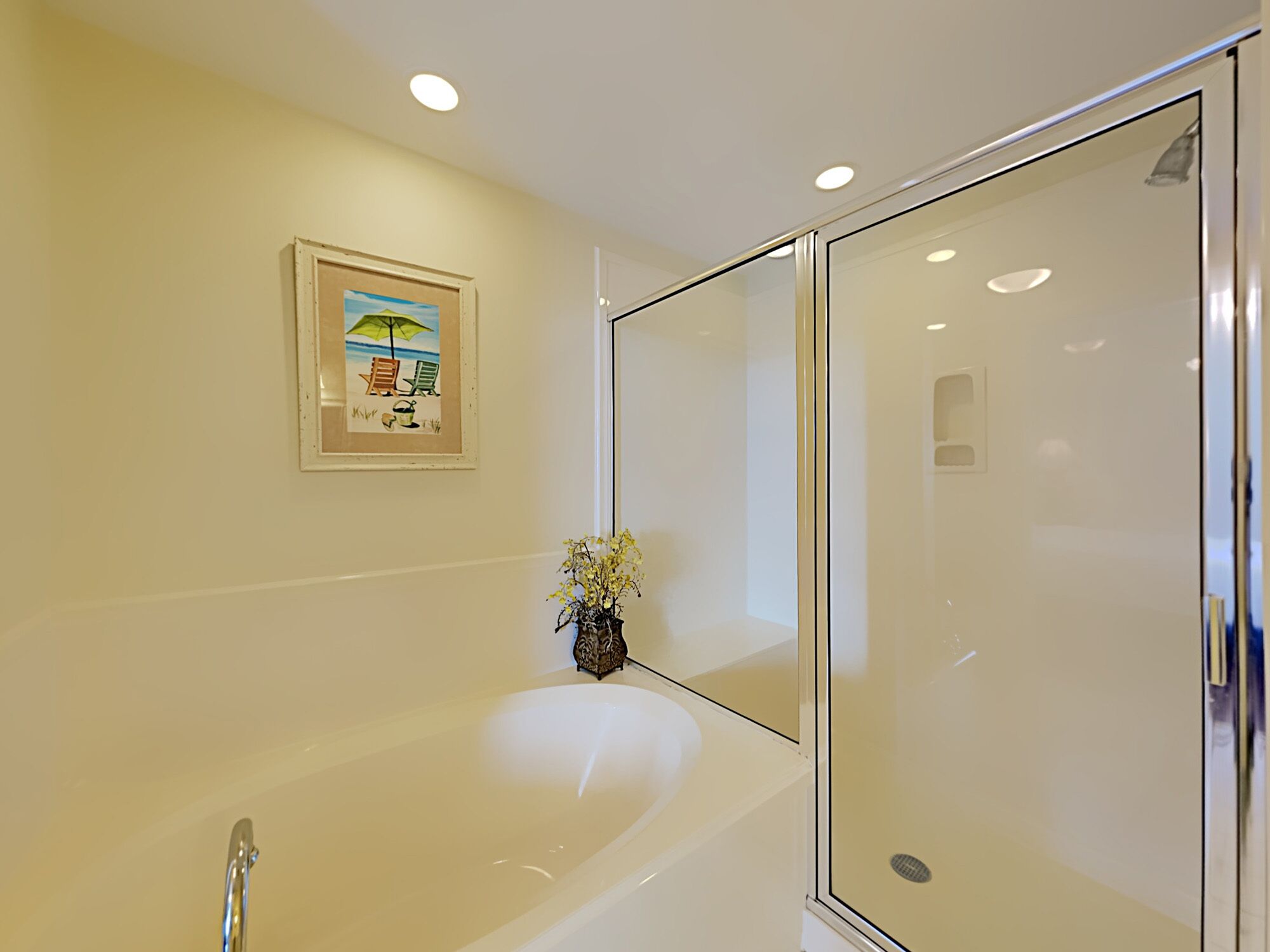 A modern bathroom with a large bathtub, a glass shower enclosure, and a framed beach scene on the wall.