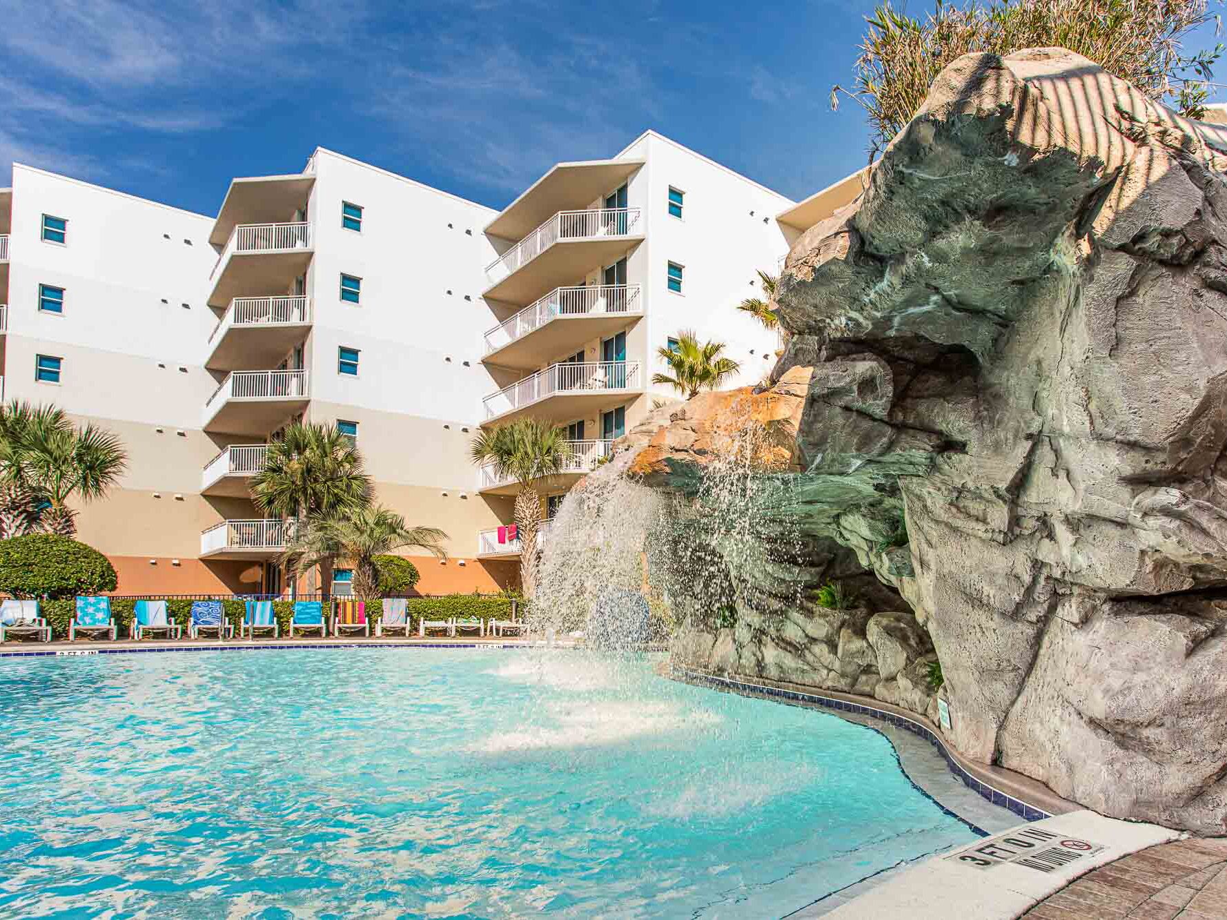 A hotel with a pool, a rock formation, and a white building with balconies.