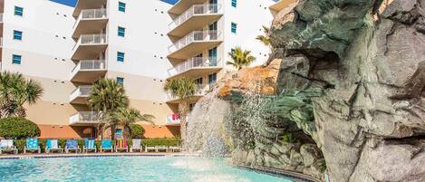 A hotel with a pool, a rock formation, and a white building with balconies.