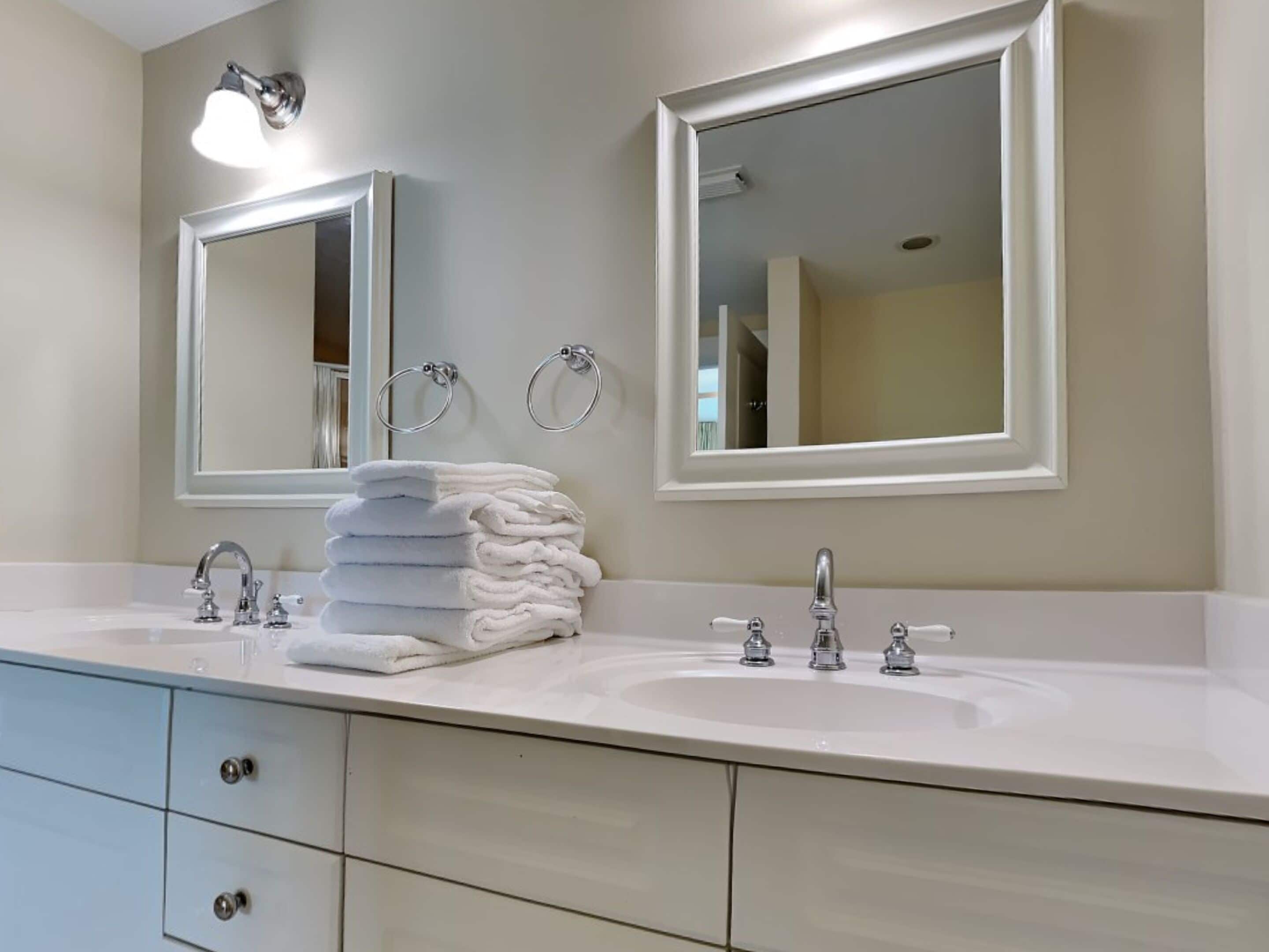 A bathroom with two sinks, a mirror, and a stack of towels.