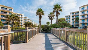 A wooden boardwalk leading to a beachfront hotel with multiple balconies and palm trees. - Waterscape by Southern Vacation Rentals (Fort Walton Beach)