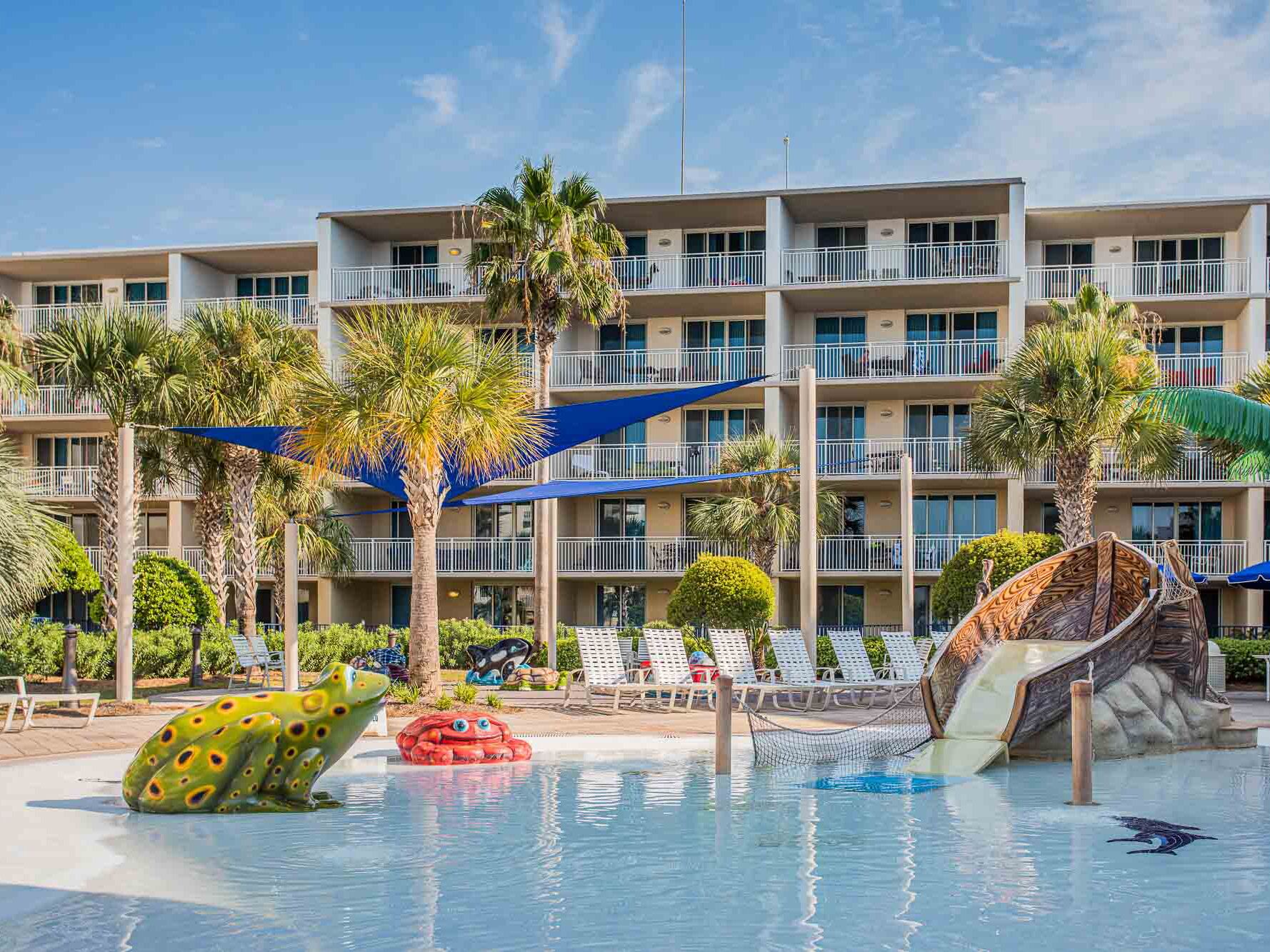 Un hotel con piscina, dotato di scivoli e giochi gonfiabili, circondato da palme e lettini.