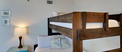 Una cama litera con estructura de madera, una mesita de noche con lámpara y dos cuadros enmarcados en la pared.