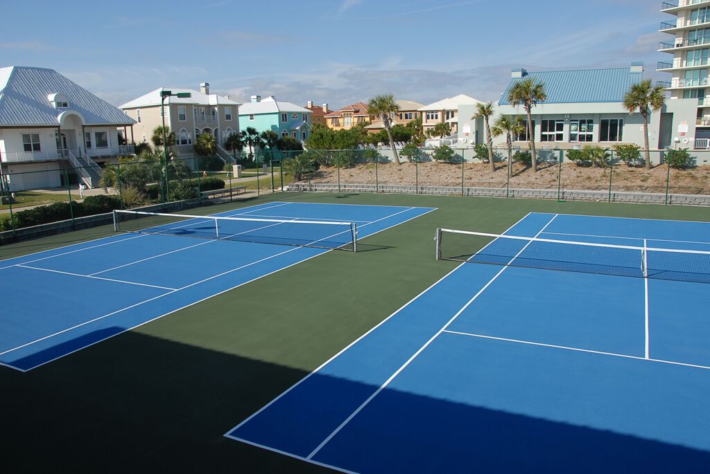 A tennis court with two courts, surrounded by buildings and palm trees.