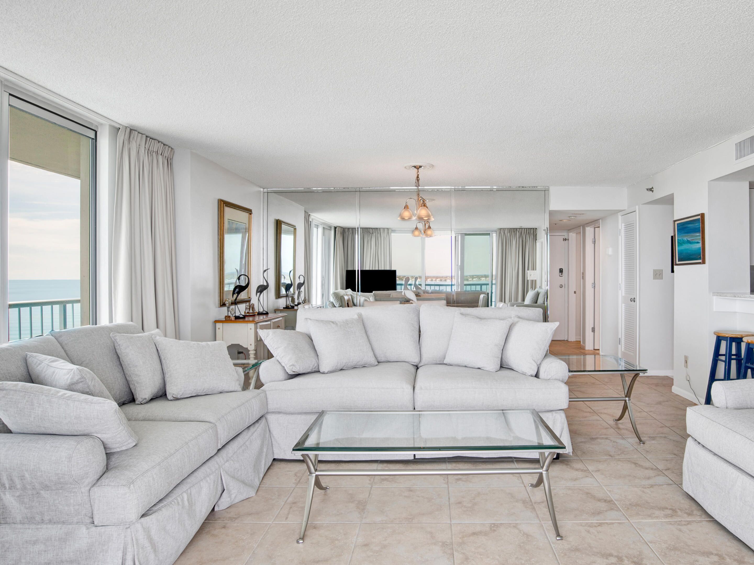 A modern living room with a large L-shaped sectional sofa, a glass coffee table, and a view of the ocean through large windows.