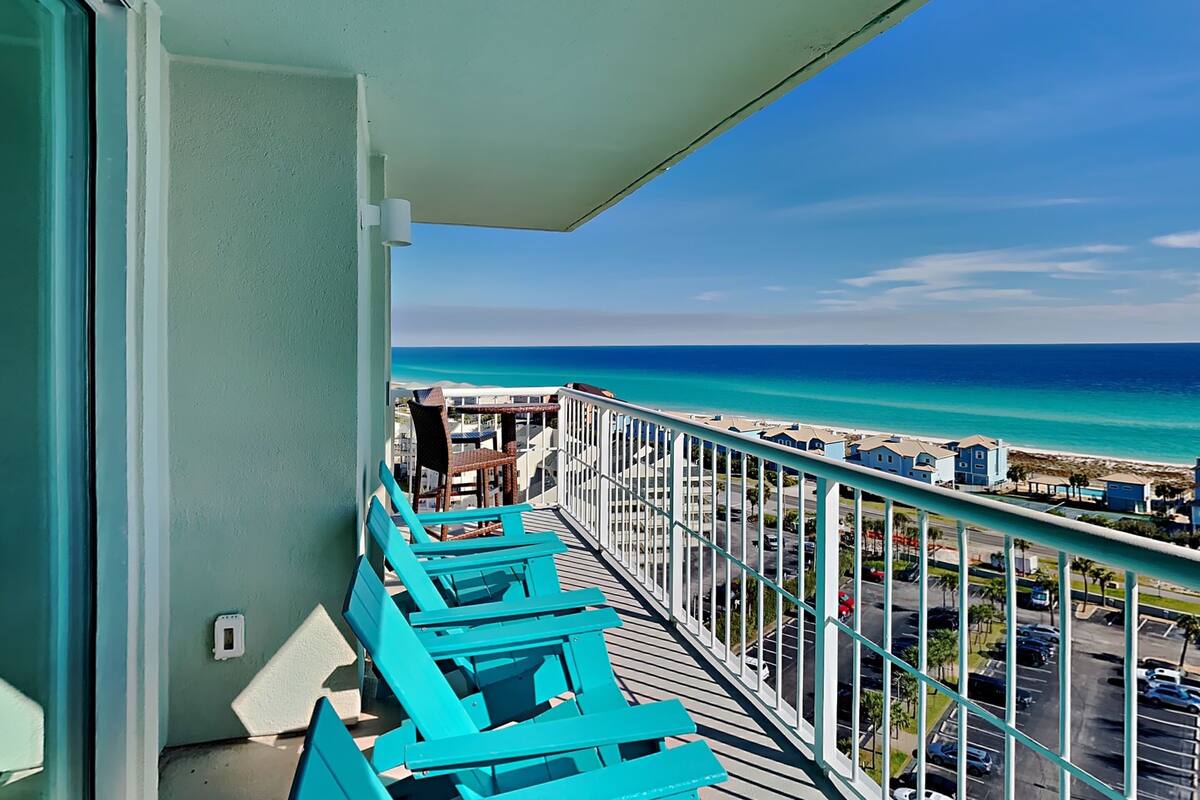 Un balcon avec des chaises turquoise donnant sur une plage et l’océan.