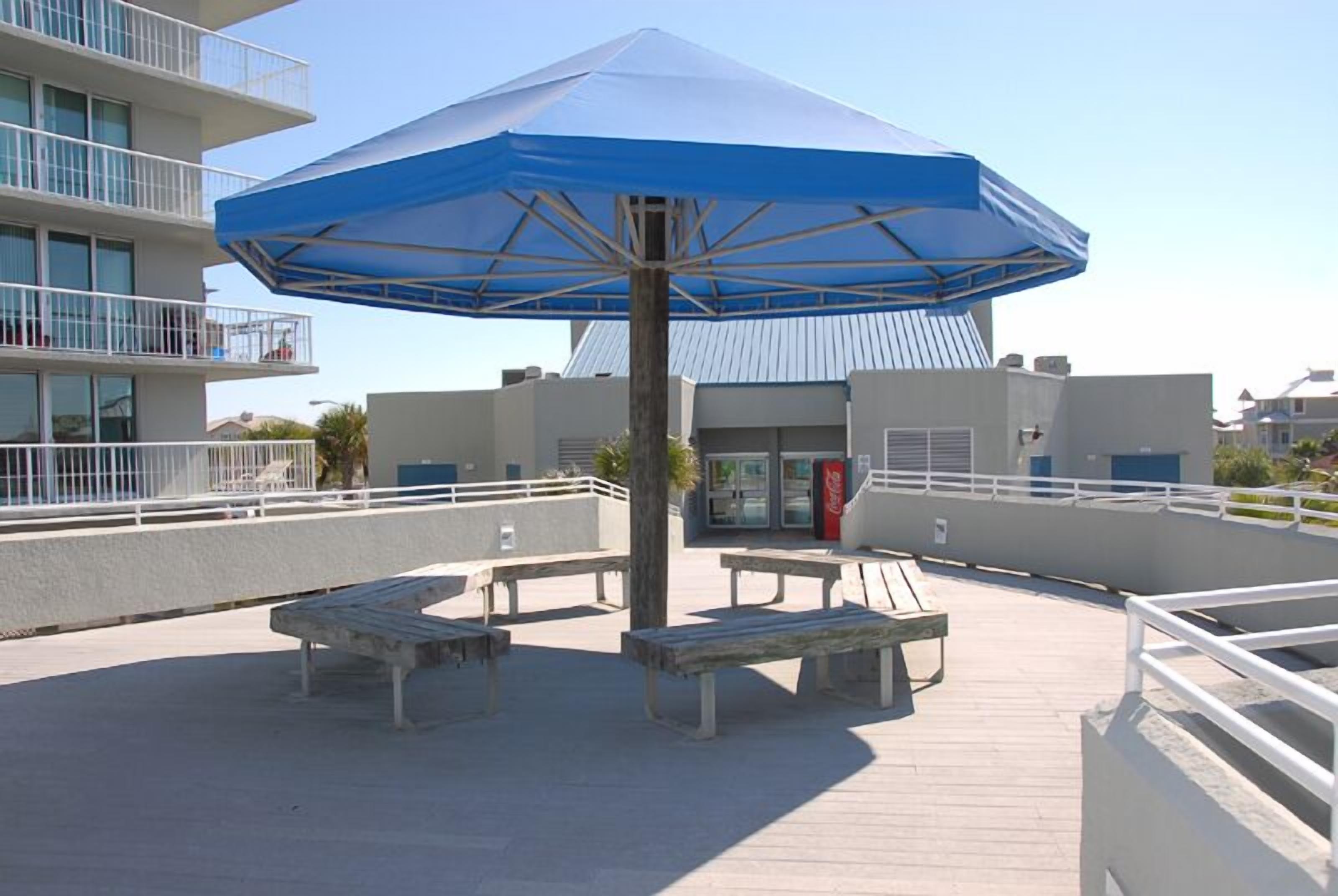 Eine Dachterrasse mit blauem Sonnenschirm, Holzbänken und einer Coca-Cola-Getränkeautomaten.