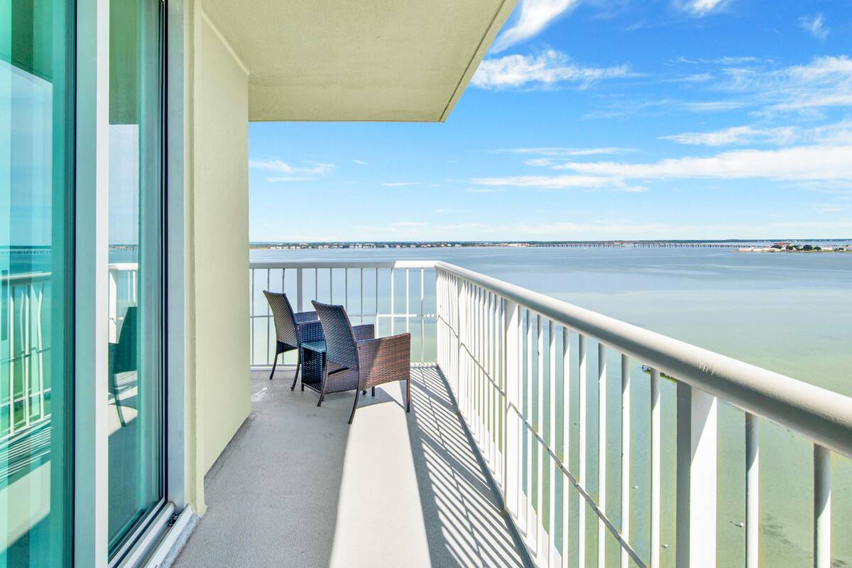 Un balcon avec deux fauteuils en osier, une porte vitrée et une vue sur l’eau et un quai.