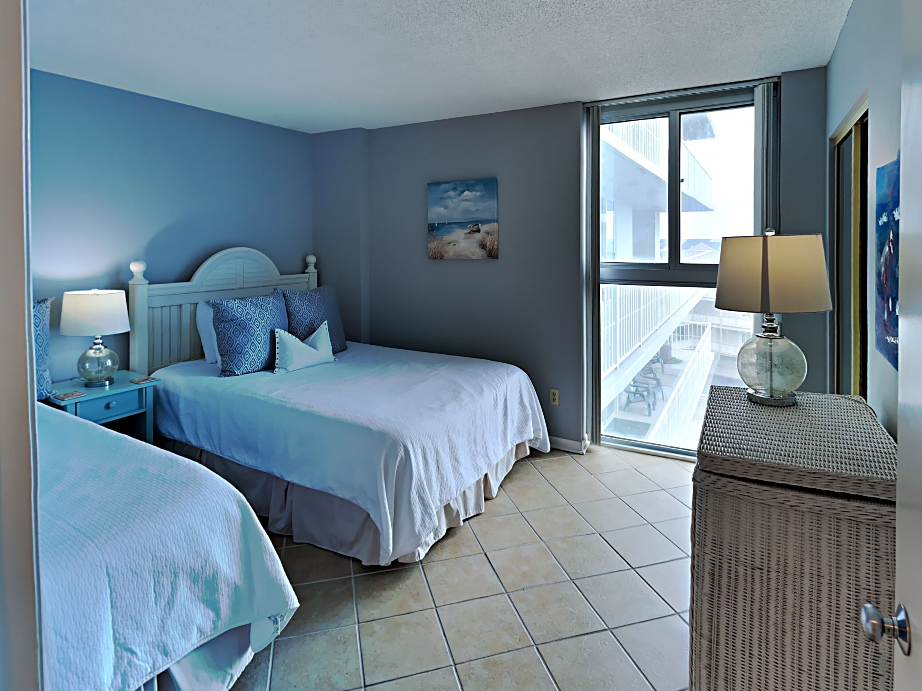 A bedroom with two beds, a balcony, and a view of the sea.