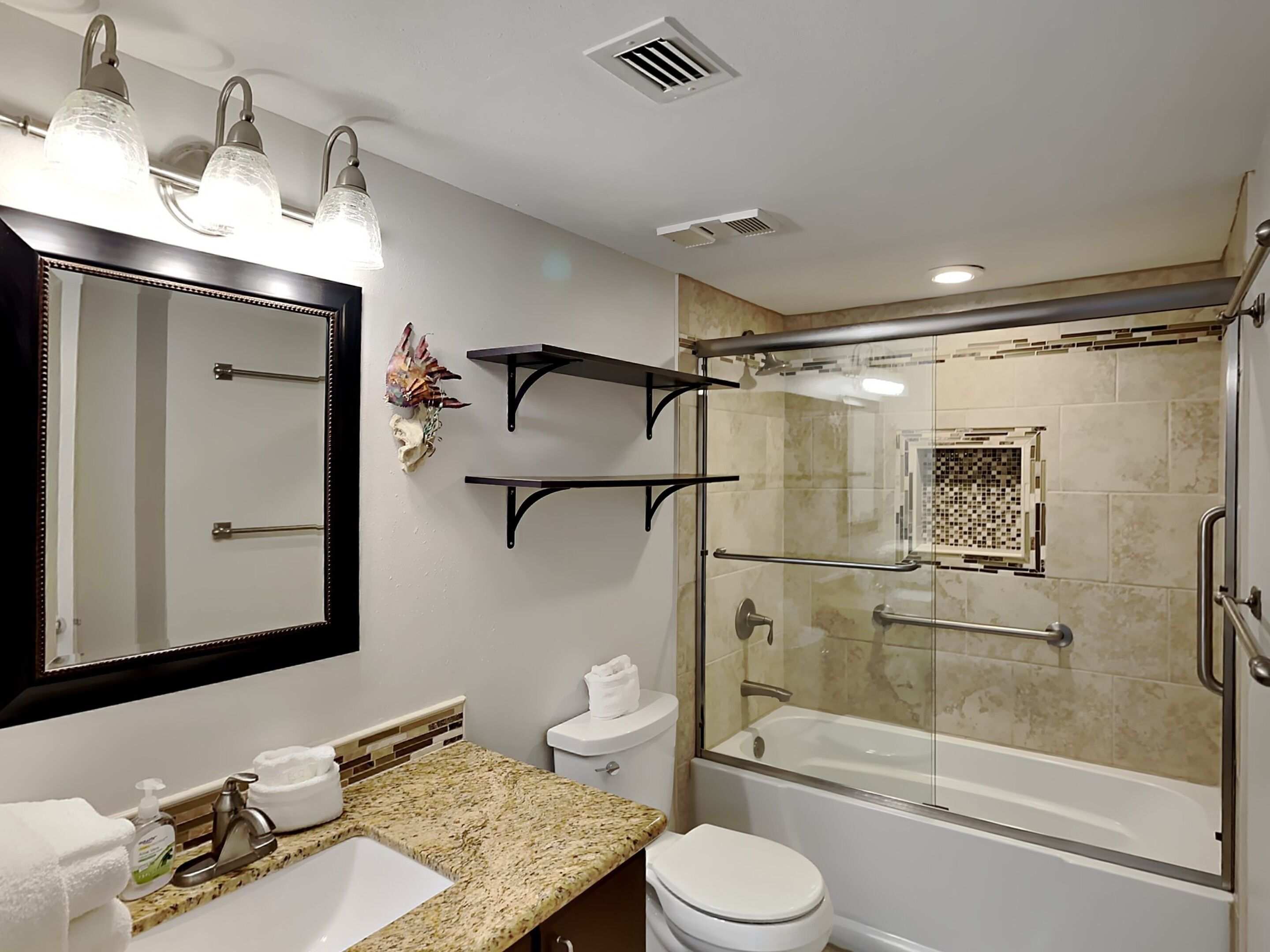A bathroom with a large mirror, a sink, a toilet, and a glass-enclosed shower area.