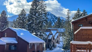 A wooden cabin with a snow-covered roof, surrounded by tall pine trees and a mountain in the background. - Pet-Friendly 5-Star Townhome, Private Hot Tub, Gas Grill, Walk to The Village (Mammoth Lakes)