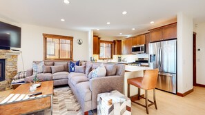 Cozy living area with a fireplace, sectional sofa, and wooden coffee table. The kitchen features stainless steel appliances and wooden cabinets.