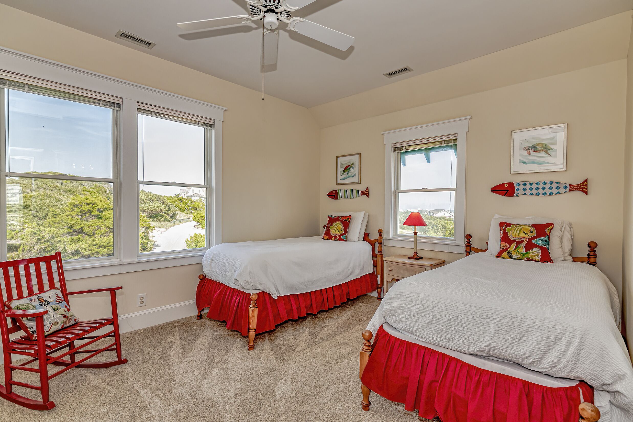 A bedroom with two beds, a rocking chair, and large windows.