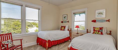 A bedroom with two beds, a rocking chair, and large windows.