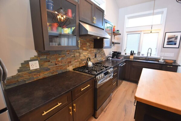 A modern kitchen with a stone backsplash, stainless steel appliances, and wooden cabinets.