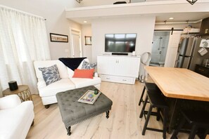 Een moderne woonkamer met een bank, voetenbankje en een eethoek met een tafel en stoelen.
