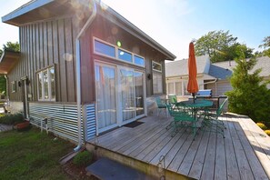 Een houten terras met een tafel en stoelen, een overdekte patio en een huis met grote ramen en een schuifdeur.